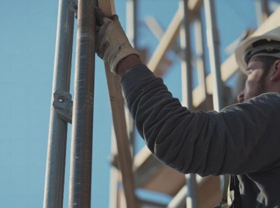 construction worker climbing a scaffold in a blue sky setting using safety gear for elevated work